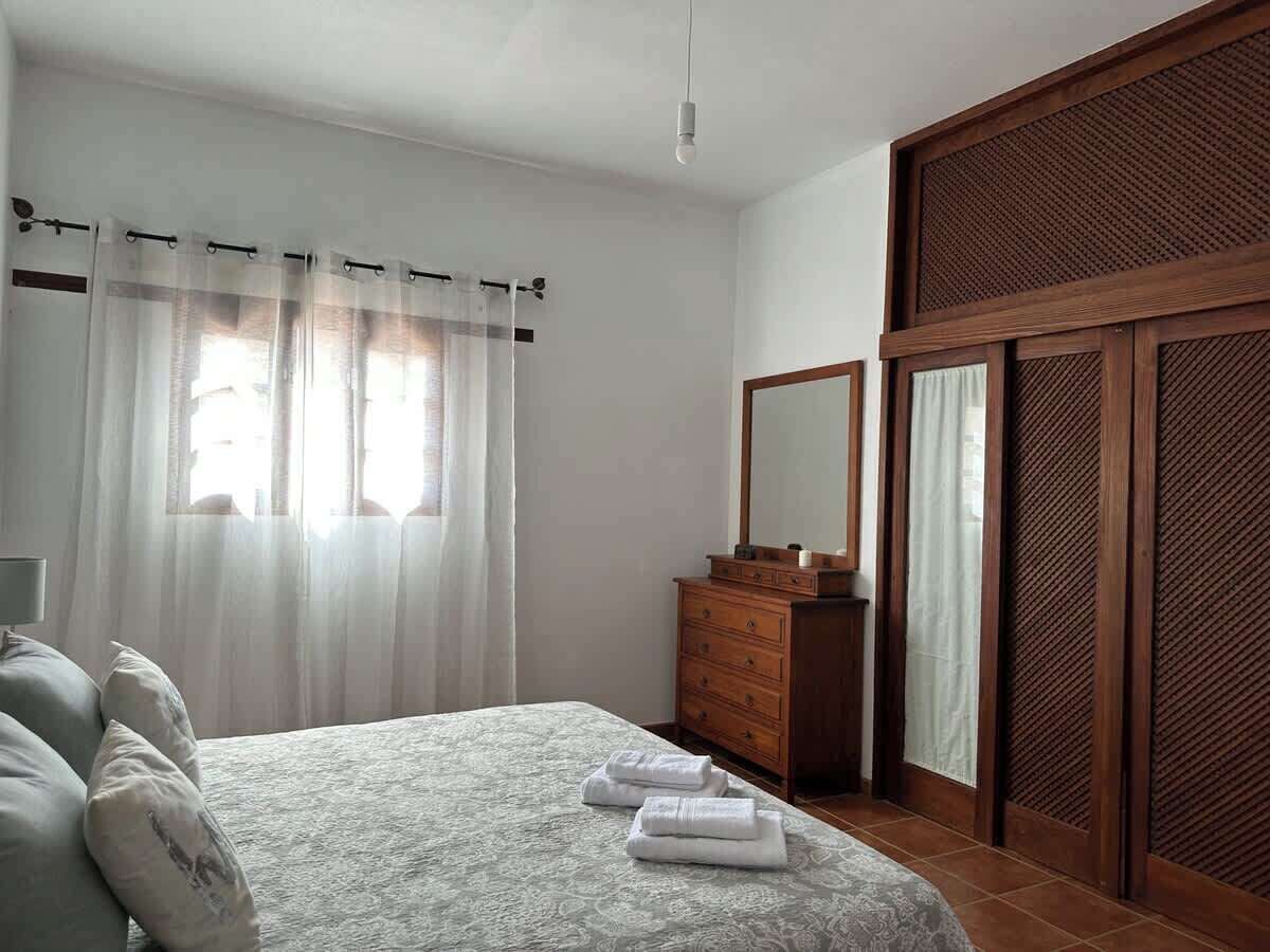 A bedroom with a bed, a wooden dresser, a mirror, and a sliding door.