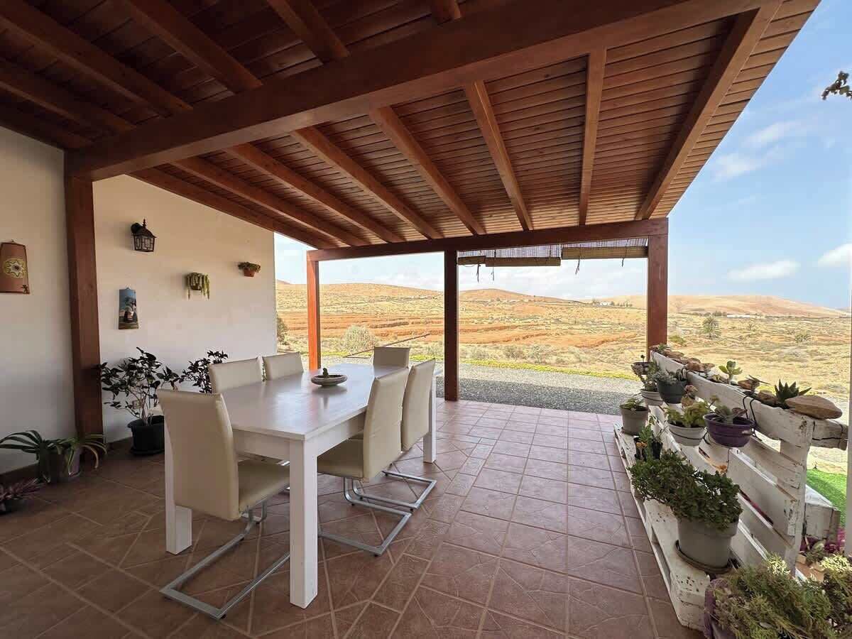 Une terrasse couverte avec une table et des chaises, entourée de plantes en pot et offrant une vue sur un paysage vallonné.