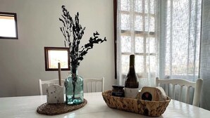Una mesa de comedor con un jarrón de flores secas, una vela y una cesta de pan.