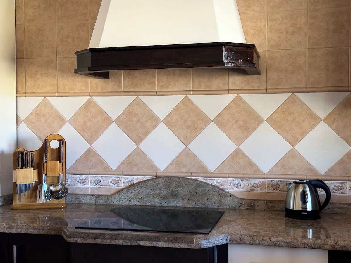 A kitchen with a tiled backsplash, a wooden utensil holder, a cutting board, and a kettle.