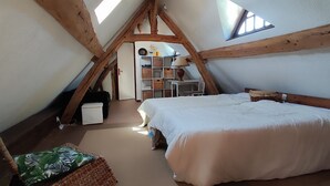 Een gezellig slaapkamer op zolder, met schuine plafonds, een bed, een stoel en een klein bureau met lamp.