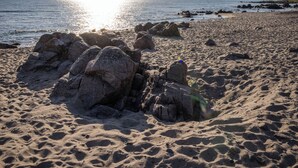 Μια παραλία με βράχια και άμμο, κάτω από έναν καθαρό ουρανό.