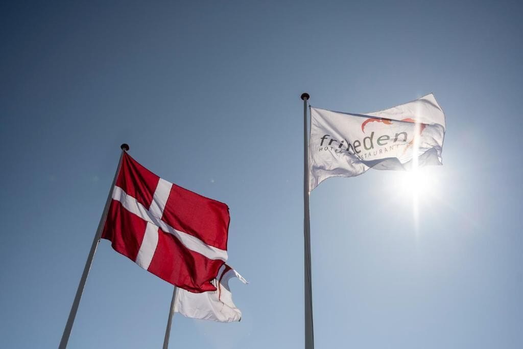Zwei Flaggen, eine Dänemarksflagge und eine mit dem Schriftzug 'freden'.