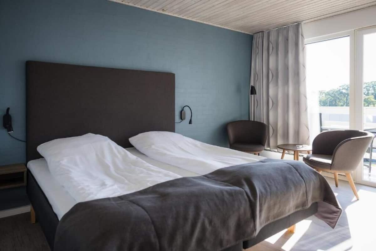 A hotel room with a large bed, a chair, a small table, and a view of the outdoors.