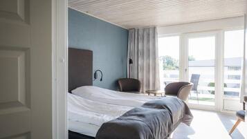 Habitación de hotel moderna con cama, una silla, una mesita y un ventanal grande con vistas al exterior.