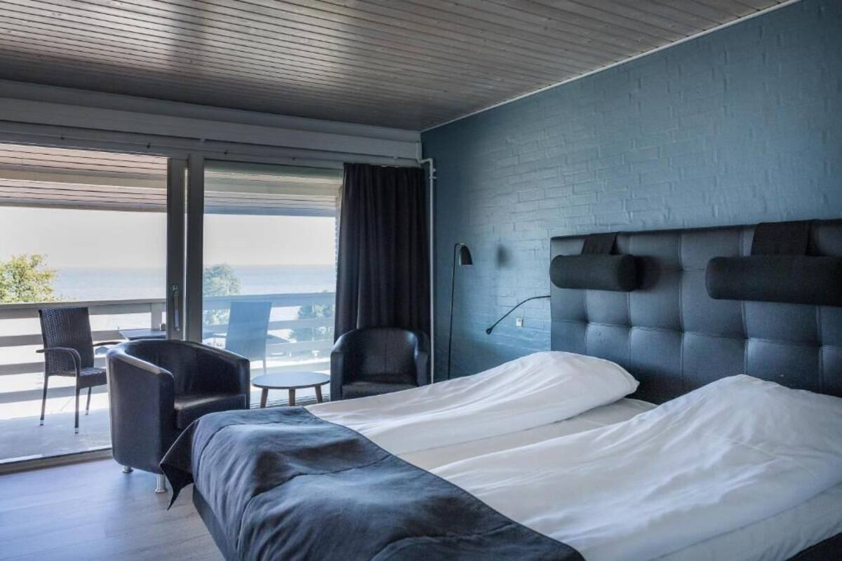 A modern hotel room with a large bed, a balcony with seating, and a view of the outdoors.