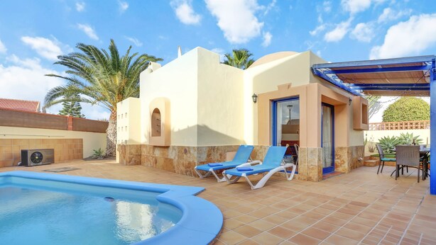Ein Swimmingpool mit blauen Fliesen, zwei Liegestühlen und einer überdachten Terrasse.