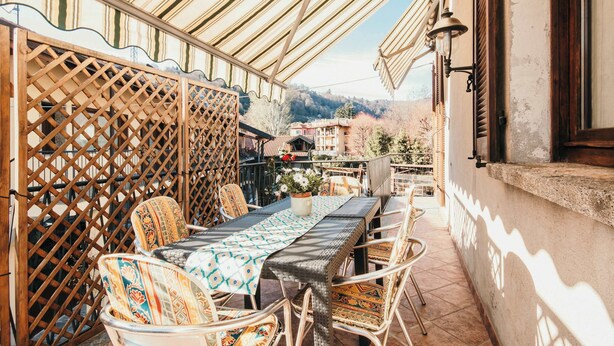 Un patio al aire libre con mobiliario de mimbre, una mesa con mantel estampado y vista a edificios al fondo.