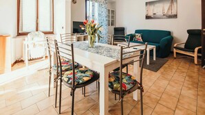 Un comedor con una mesa, sillas y un jarrón de flores. Hay un televisor, un sofá y un cuadro en la pared.