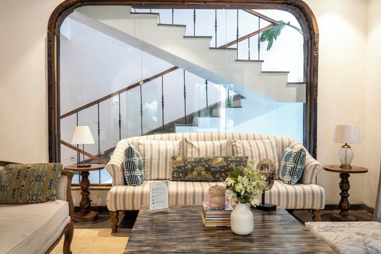 Ein Wohnzimmer mit einem gestreiften Sofa, einem Couchtisch mit Büchern und einer Vase sowie einer Treppe im Hintergrund.