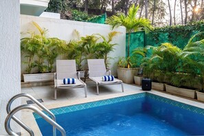 Un área junto a la piscina con sillones de descanso y plantas en macetas.