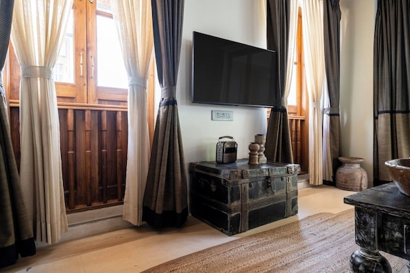 Una habitación con una televisión en la pared, un cofre de madera y cortinas.
