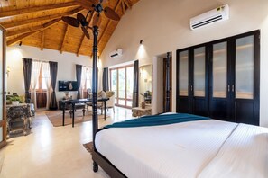 Ein Hotelzimmer mit einem großen Bett, einem Deckenventilator, einer Klimaanlage, einem Fernseher und einer Schiebetür, die auf einen Balkon führt.