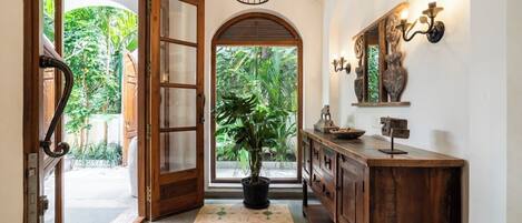 A hallway with a wooden door, a potted plant, a console table with a mirror, and a patterned rug.