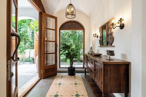 A hallway with a wooden door, a potted plant, a console table with a mirror, and a patterned rug. - Staymaster Stardust 3BHK Vagator  (Vagator)