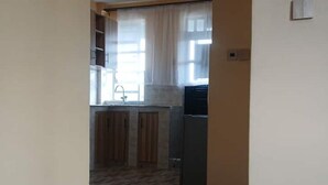A kitchen with a refrigerator, wooden cabinets, and a window with curtains. - Stacy's Cozy Bed and Breakfast in Nakuru, Kenya (Nakuru)