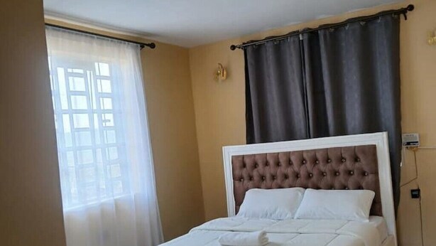 A hotel room with a bed, curtains, and a window. - Stacy's Cozy Bed and Breakfast in Nakuru, Kenya (Nakuru)