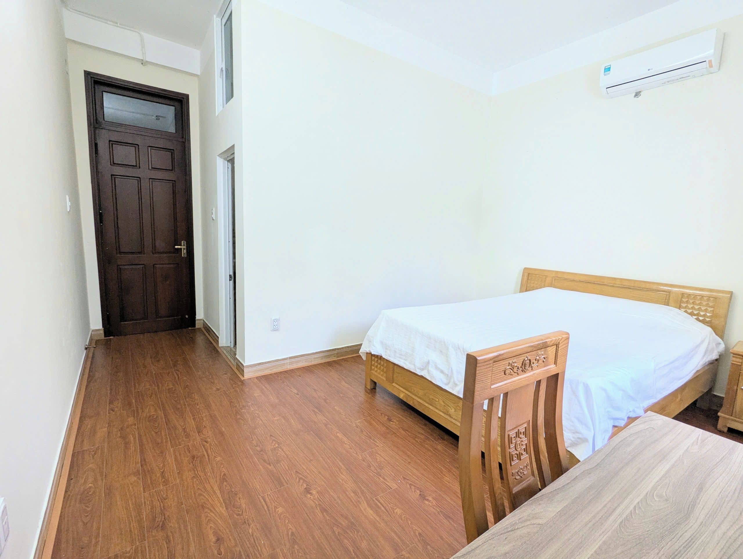 Een kamer met een houten deur, een bed met een houten hoofdeinde en een airconditioning op de muur.