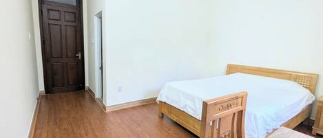 Een kamer met een houten deur, een bed met een houten hoofdeinde en een airconditioning op de muur.