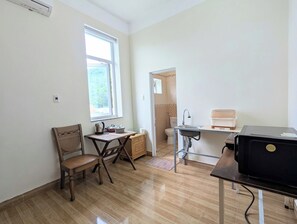 A compact room with a wooden chair, a small table, a window, a sink, and a black appliance. - AN Apartment (Son Tra)