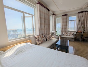A hotel room with a bed, a sofa, a chair, and a table. There are large windows with curtains. - AN Apartment (Son Tra)