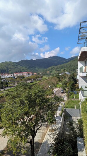 A residential area with a view of a mountain range, a paved road, and a building with a modern design. - AN Apartment (Son Tra)