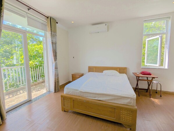 A bedroom with a bed, a small table, a nightstand, a window, and a balcony. - AN Apartment (Son Tra)