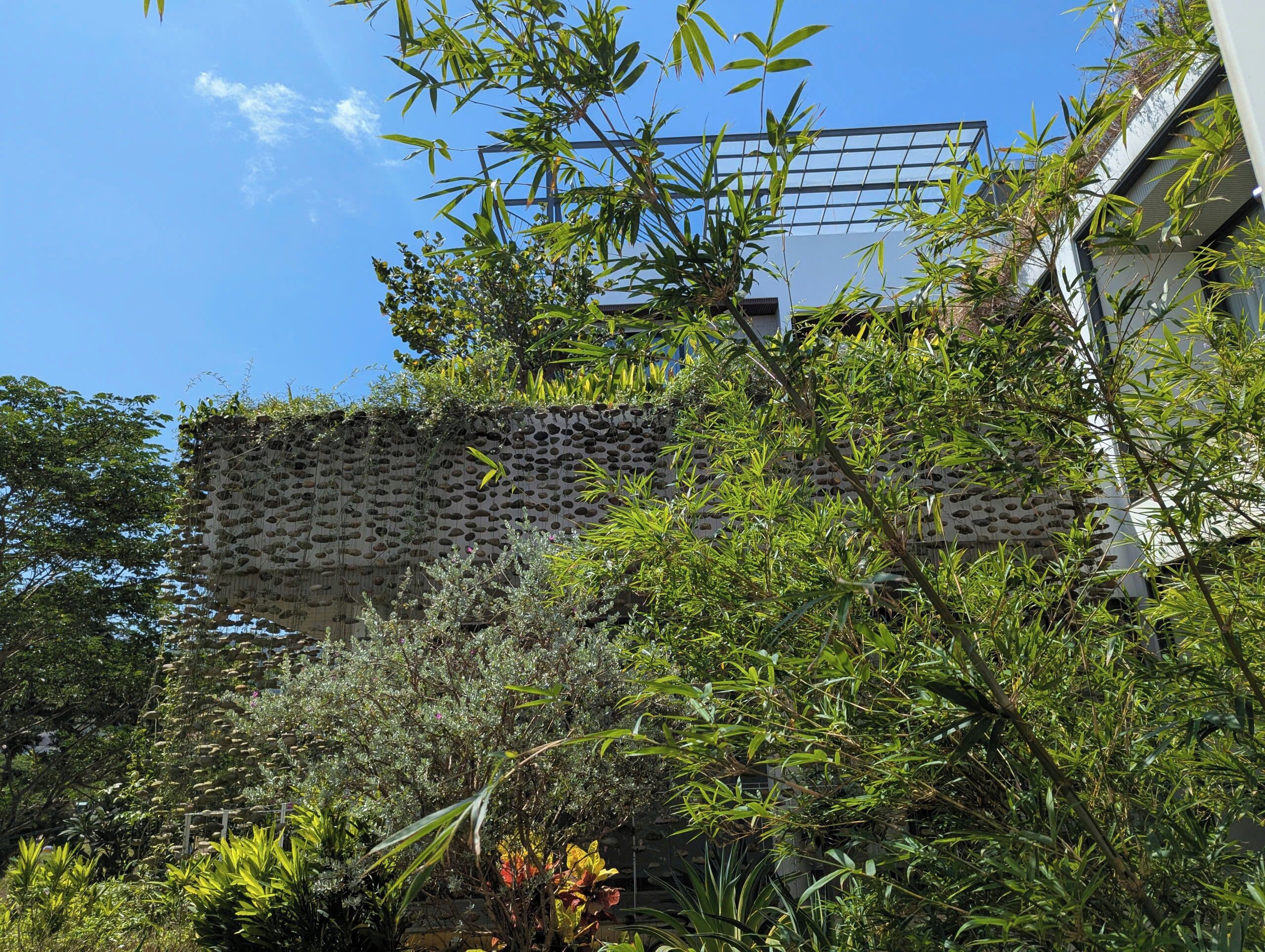 A building with a unique perforated facade, surrounded by dense foliage and trees.