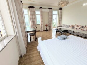 A hotel room with a bed, a sofa, a dining table with chairs, and a balcony with curtains. - AN Apartment (Son Tra)