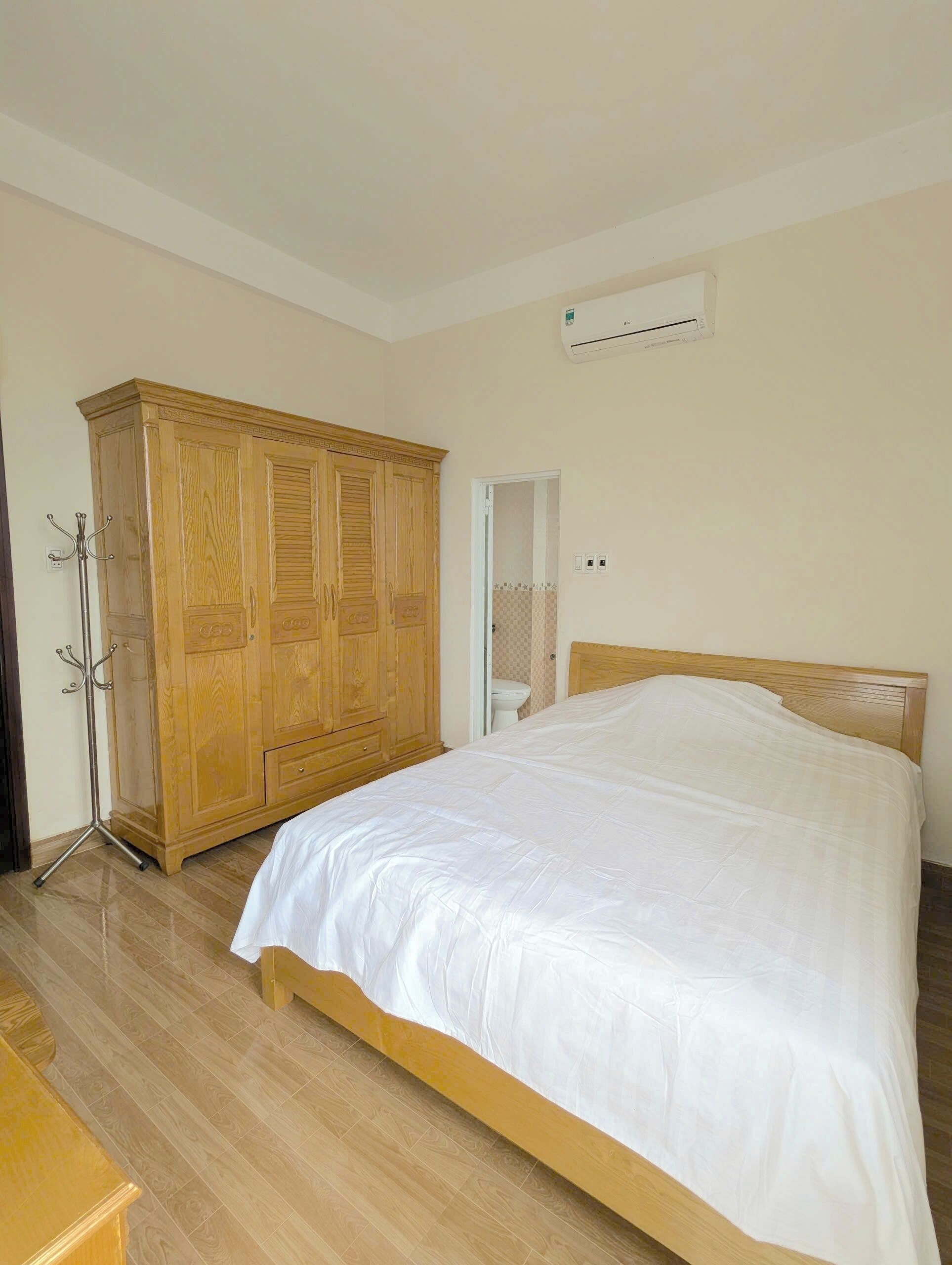 Un dormitorio con un armario de madera, una cama con ropa de cama blanca y un equipo de aire acondicionado en la pared.