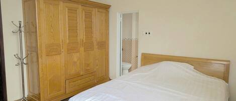 Un dormitorio con un armario de madera, una cama con ropa de cama blanca y un equipo de aire acondicionado en la pared.