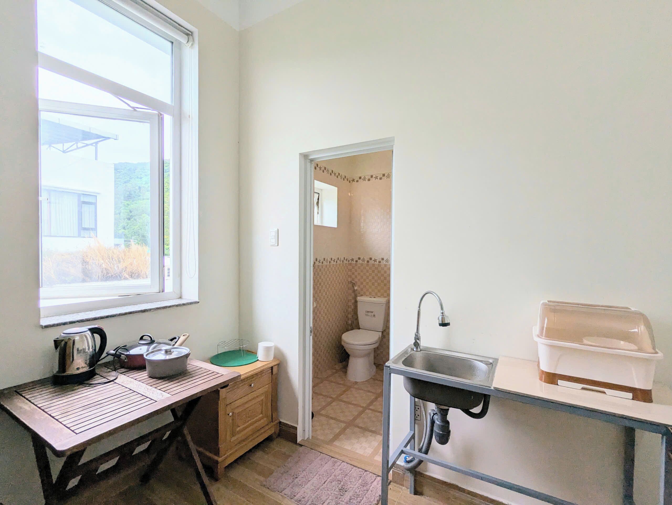 A compact kitchen with a window, a sink, a countertop, and a small table with kitchenware.
