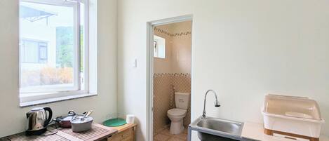 A compact kitchen with a window, a sink, a countertop, and a small table with kitchenware.