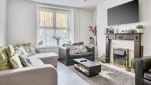 Una sala de estar con chimenea, sofá, mesa de centro y televisor montado en la pared.