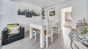 Una sala de estar moderna con una mesa de comedor, sillas blancas, un sofá negro y un sillón estampado.