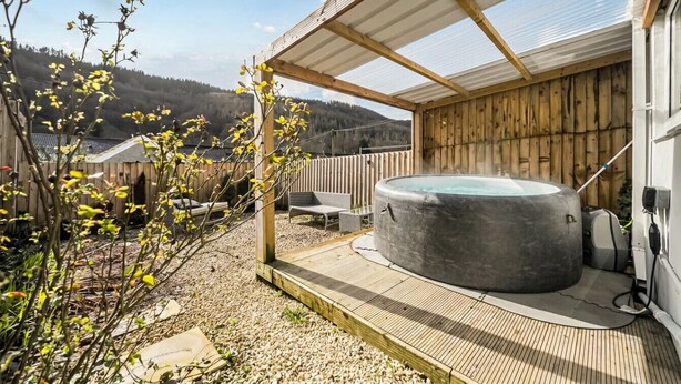 Un jacuzzi bajo una pérgola de madera con vista a un promontorio boscoso.
