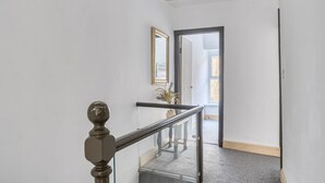 Una escalera con barandilla de vidrio, pasamanos de madera y una lámpara colgante.