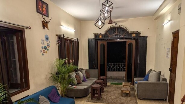 Un salon avec un canapé bleu, un canapé gris et une petite table en bois. On y trouve des plantes en pot et une décoration murale.