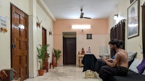 Une pièce avec un lit, une petite table, une plante en pot et un ventilateur de plafond.