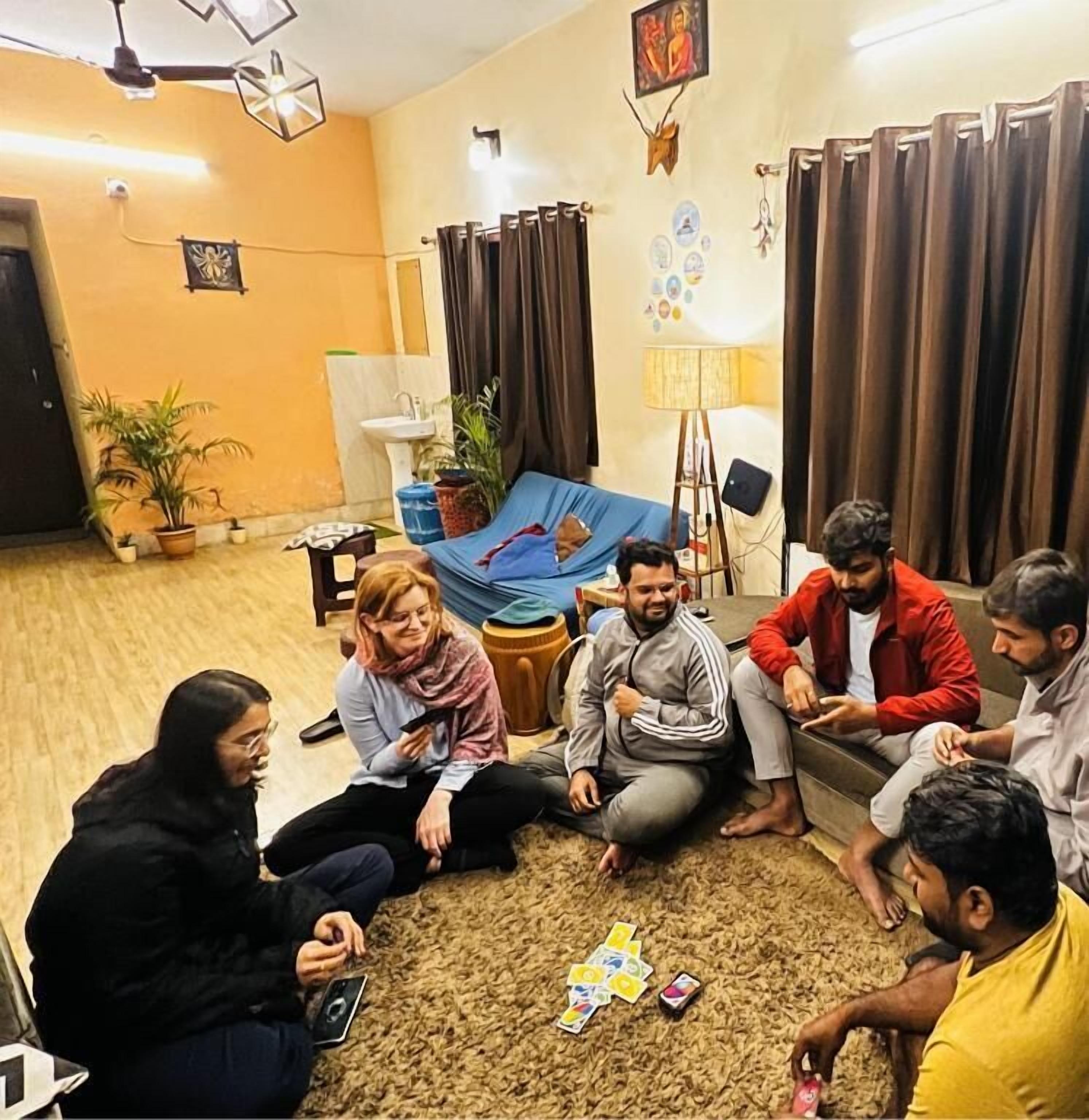 Un gruppo di persone sedute sul pavimento in un soggiorno con un divano blu, una lampada e una pianta.