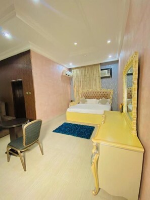 A hotel room with a bed, a desk, a chair, and an air conditioning unit on the wall. - GARDEN ATLANTIS HOTEL (Enugu)