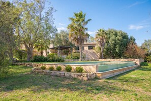 Piscina com borda de pedra, rodeada por grama e árvores.