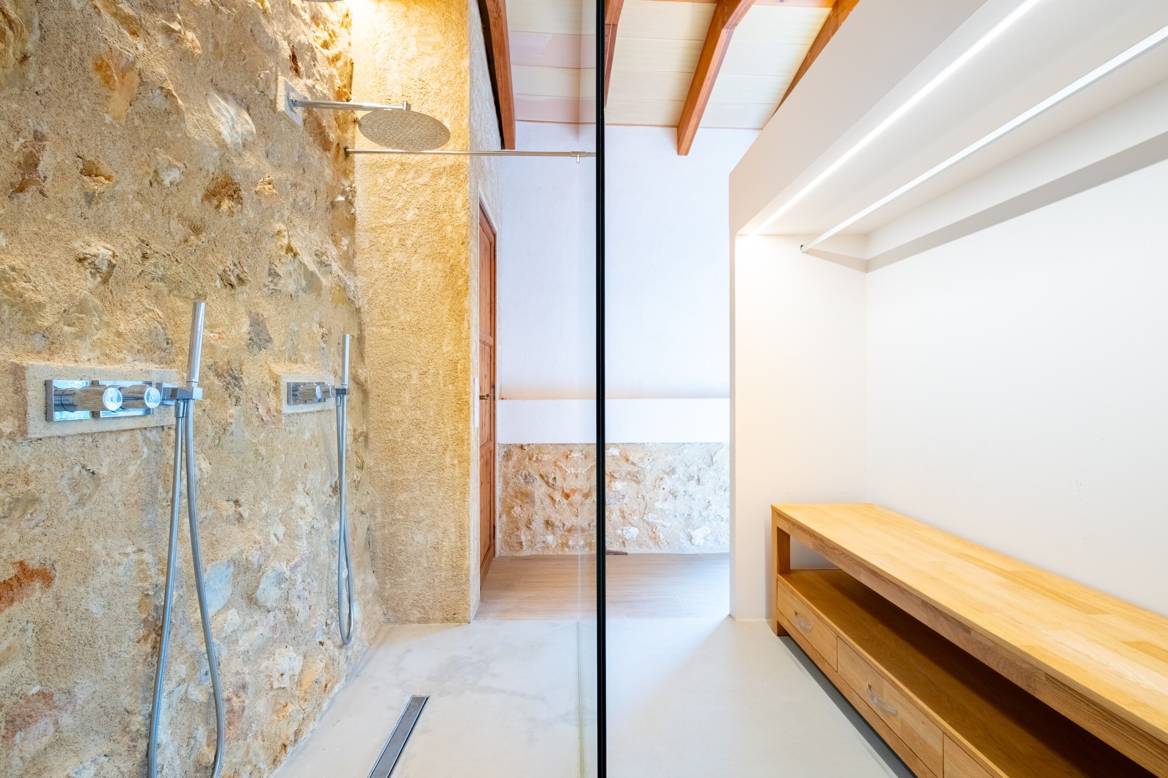 A modern bathroom with a stone wall, a shower, and a wooden bench.