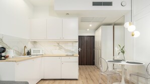 Una cocina moderna con armarios blancos, encimera de mármol y zona de comedor con sillas traslúcidas y una mesa blanca.