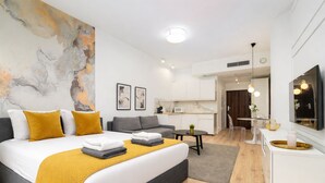 Una habitación de hotel moderna con cama, sofá, kitchenette y un cuadro abstracto grande en la pared.