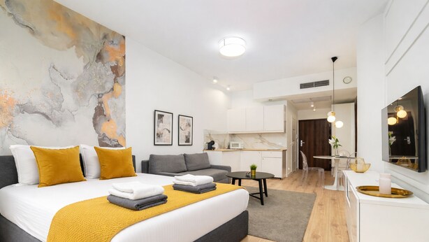 Una habitación de hotel moderna con cama, sofá, kitchenette y un cuadro abstracto grande en la pared.