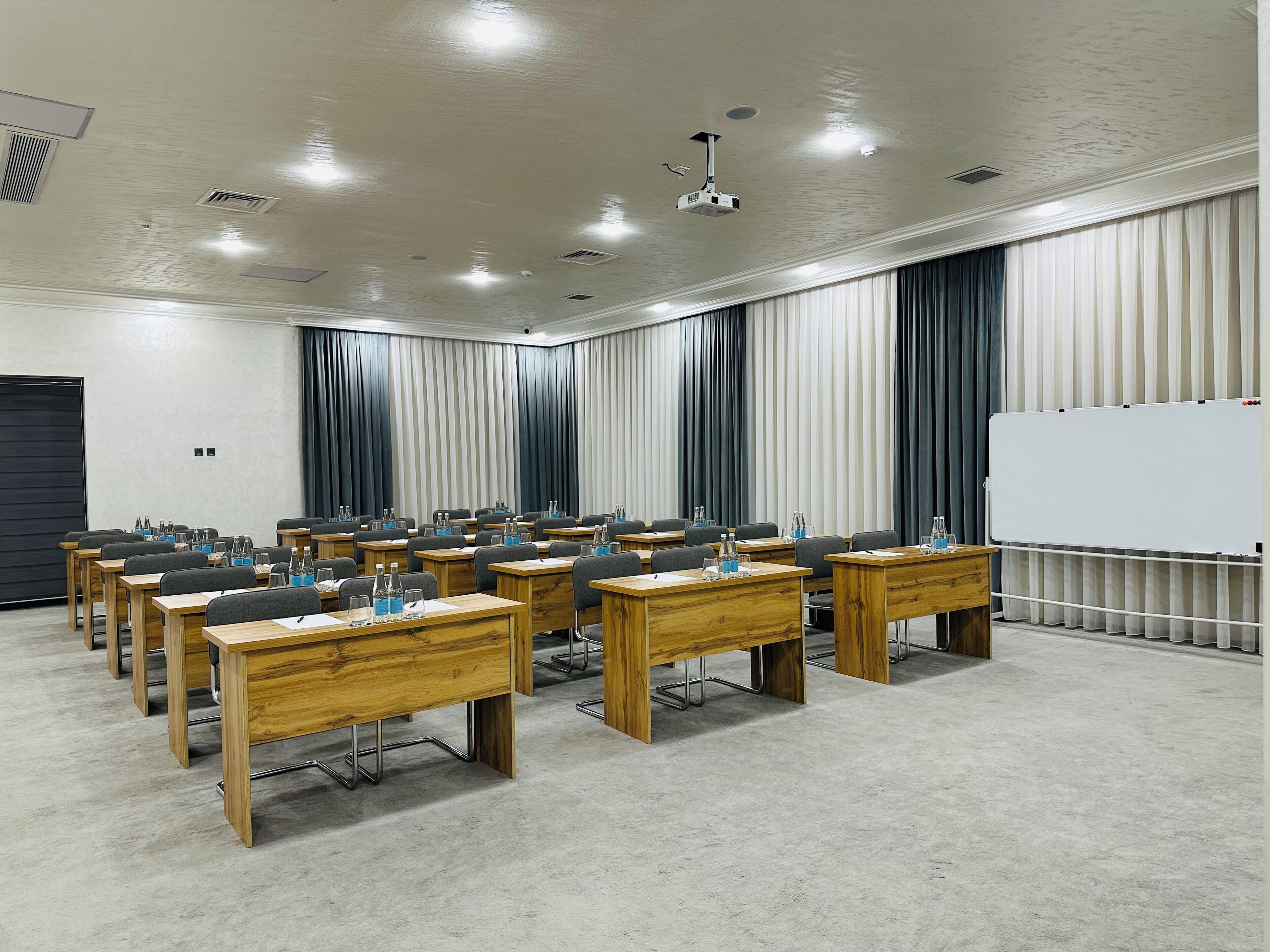 Ein Konferenzraum mit Holztischen, Stühlen, einer Tafel und einem Projektor.