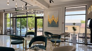 Een modern interieur met ronde tafels, stoelen en een groot raam met uitzicht op geparkeerde auto's en groen.