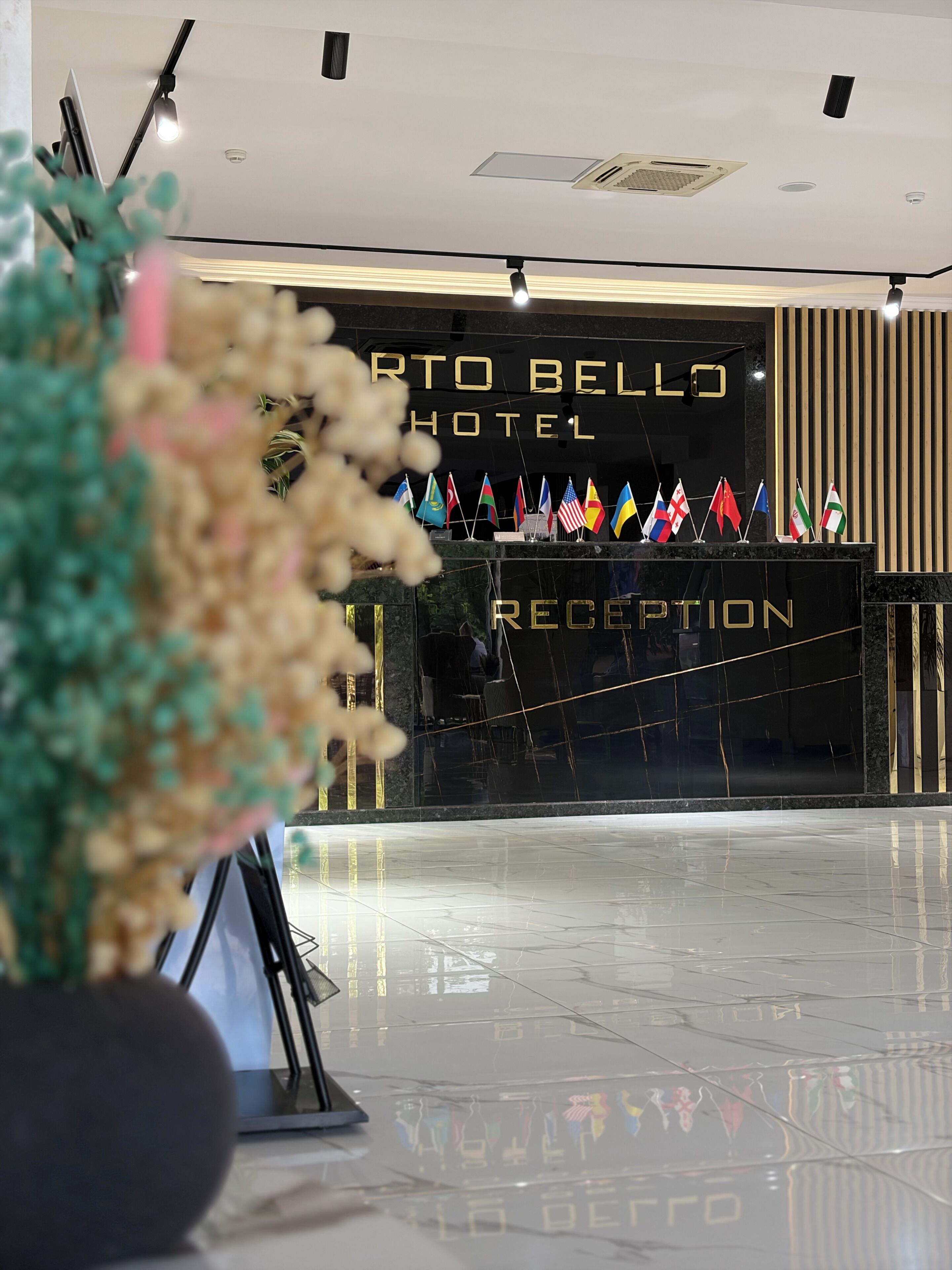 Área de recepção de hotel com design moderno, destacando um balcão de atendimento, bandeiras e piso lustroso.