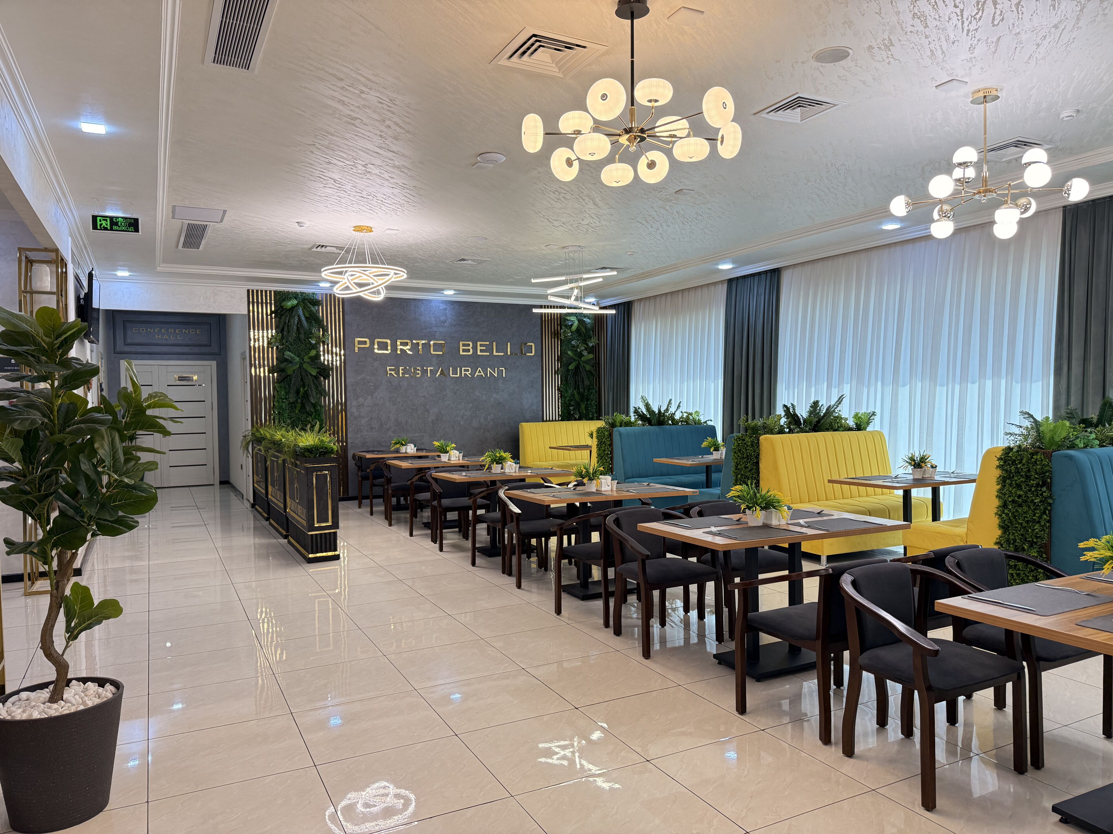 Een restaurantinterieur met tafels, stoelen, plafondlampen en een bord waarop 'PORTO BELLO RESTAURANT' staat.